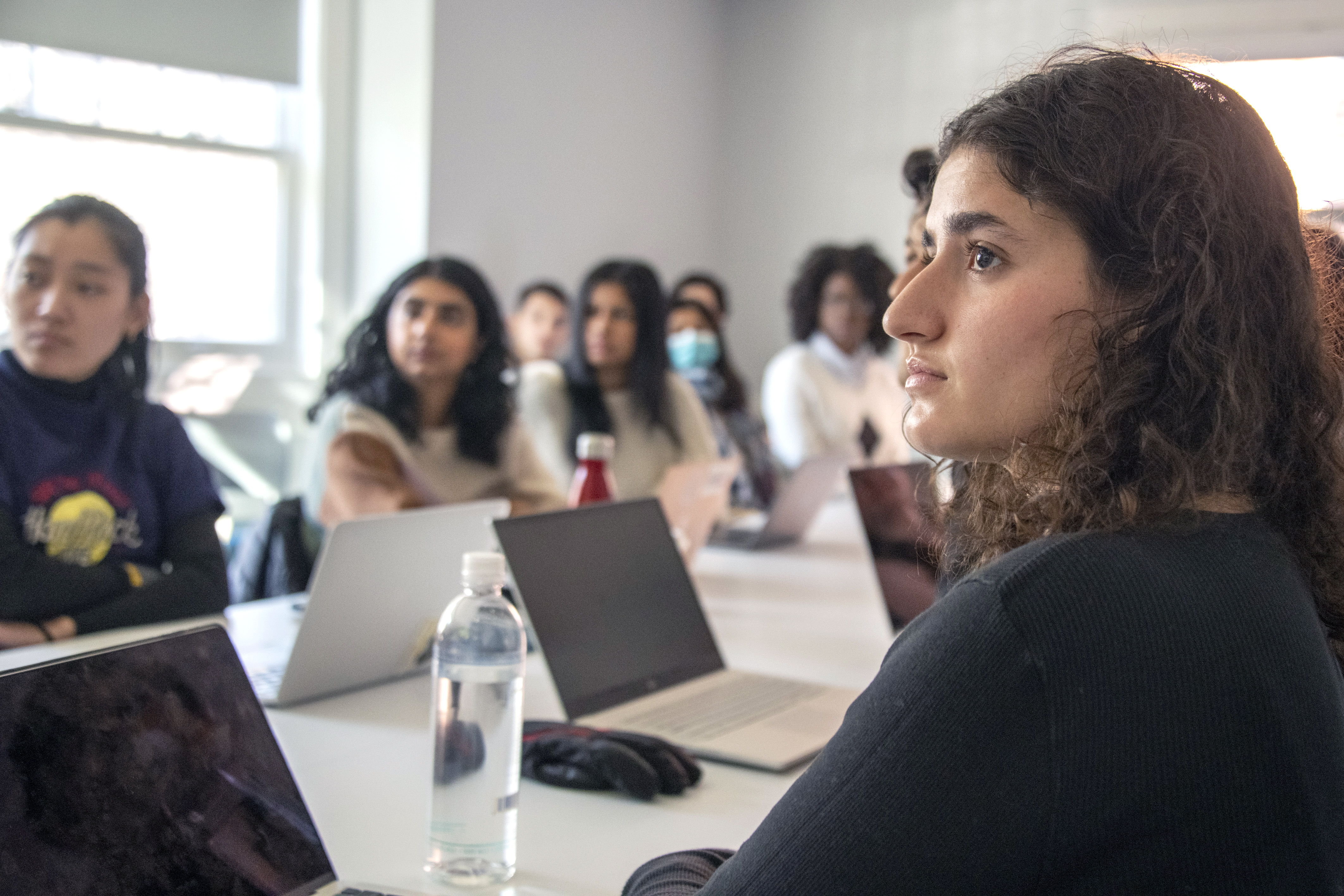 photo of students in a class. Girl with brown hair and brown eyes looking at the offscreen presenter